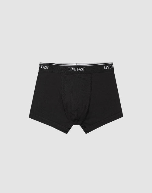 A pair of black Live Fast Trunks (2 Pack) by LIVE FAST DIE YOUNG, made from soft cotton with LIVE FAST repeatedly printed in white on the elastic waistband, displayed on a plain light gray background.