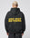 A person with short blond hair wears the LFDY Drift Hooded by LIVE FAST DIE YOUNG, a black hoodie with yellow LIVE FAST. DIE YOUNG text on the back, Oversize Fit, and doppellagige Kapuze, against a plain light background.