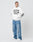 A person in a white LIVE FAST DIE YOUNG LFDY Ultra Hooded with "Nothing less but Ultra" on the front, Bündchen an Ärmeln, and oversize fit, styled with light blue ripped jeans and white sneakers, stands against a plain background looking sideways.