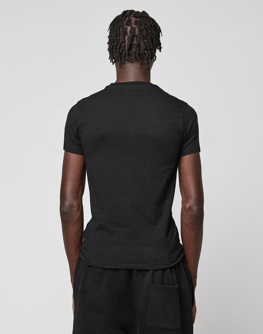 A person with short, twisted hair is shown from behind in a plain black LIVE FAST DIE YOUNG LFDY Slim Tee and black pants against a light gray background. A small Flag-Label detail completes the minimalist look.