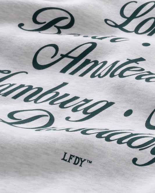 A close-up of the Rhine Area Hooded by LIVE FAST DIE YOUNG shows white Baumwolle fabric with bold black script listing cities like Amsterdam and Hamburg. The small LFDY™ text appears near the bottom of the image.