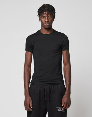 A young man with short, twisted hair wears the LFDY Slim Tee from LIVE FAST DIE YOUNG and black sweatpants, standing against a light gray background with a neutral expression.