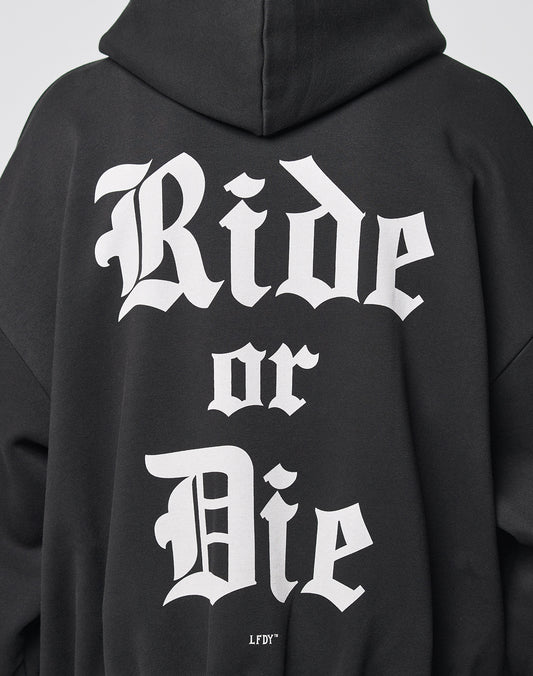 A person wearing the LIVE FAST DIE YOUNG Ride or Die Hooded Zip, a black hoodie with bold white Gothic-style Ride or Die text on the back, featuring an oversize fit and doppellagige Kapuze for comfort.