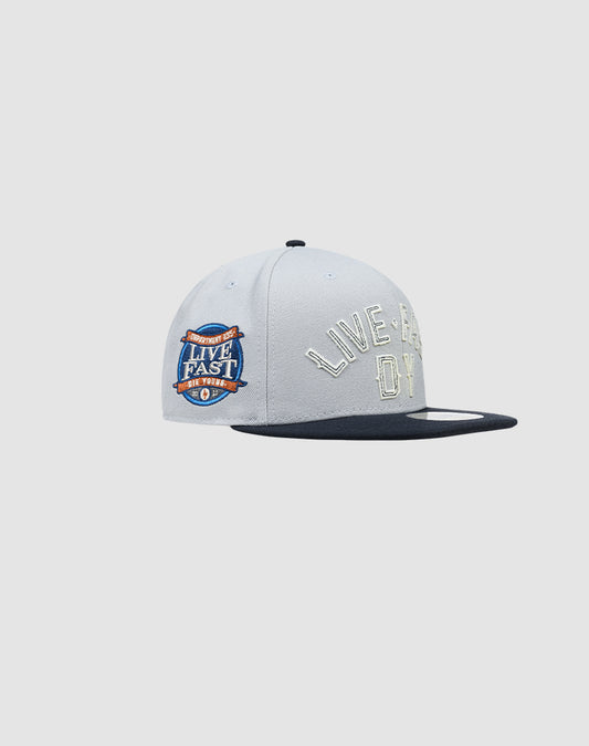 The LFDY X NEW ERA 59FIFTY by LIVE FAST DIE YOUNG is a white and black fitted cap with “LIVE FAST, DIE YOUNG” front embroidery and a colorful side patch. Displayed on a plain light background. Find your size with our Größentabelle.