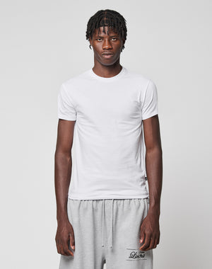 A young man with short, twisted hair wears the LIVE FAST DIE YOUNG LFDY Slim Tee in white and light gray sweatpants, standing against a plain light gray background and looking directly at the camera with a neutral expression.