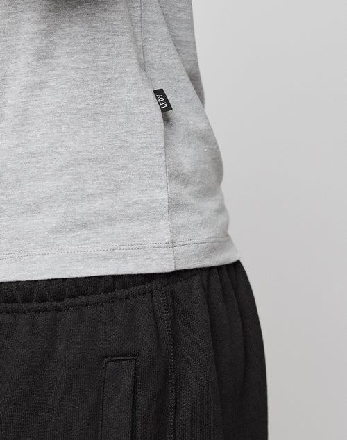 Close-up of a person wearing the LIVE FAST DIE YOUNG LFDY Slim Tee in light grey cotton with a small black flag label, paired with black sweatpants featuring an elastic waistband and pockets, set against a plain light background.