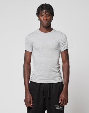 A man with short twisted hair wears a light gray LFDY Slim Tee by LIVE FAST DIE YOUNG and black drawstring pants, standing against a plain light background with a neutral expression.