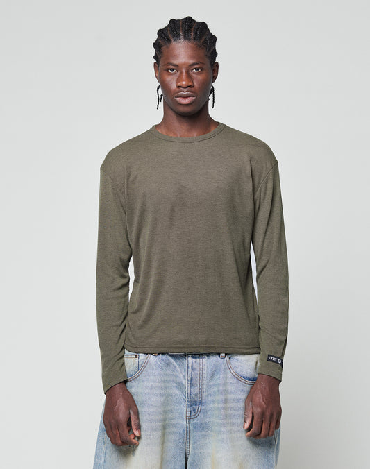 A person with braided hair wears an olive green LFDY Rib Longsleeve by LIVE FAST DIE YOUNG and light blue baggy jeans, standing against a plain light gray background.