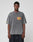 A young man with short hair and a neutral expression models the LIVE FAST DIE YOUNG LFDY Metro Boomin Tee, an oversize faded gray 100% cotton shirt with yellow and red sleeve print, paired with wide dark pants against a plain background.
