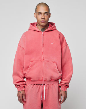 A person with a shaved head and neck tattoos wears the LIVE FAST DIE YOUNG Basic Hooded Zip and matching sweatpants in pink with a subtle fade effect, standing against a plain light gray background.