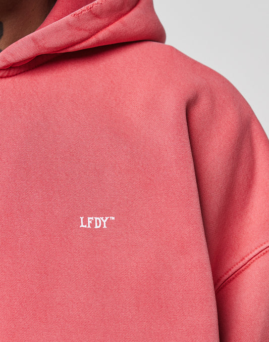 Close-up of a person wearing the LIVE FAST DIE YOUNG Basic Hooded Zip in pink, featuring a small white LFDY⢠logo print on the front and showcasing the fabricās subtle fade effect. Only part of the hoodie and their neck and chin are visible.