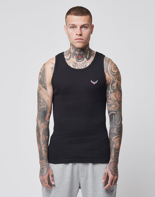 A man with short hair and extensive neck and arm tattoos wears the LFDY x Trigema Rib Tank by LIVE FAST DIE YOUNG, paired with gray sweatpants, standing against a white background and looking ahead with a neutral expression.