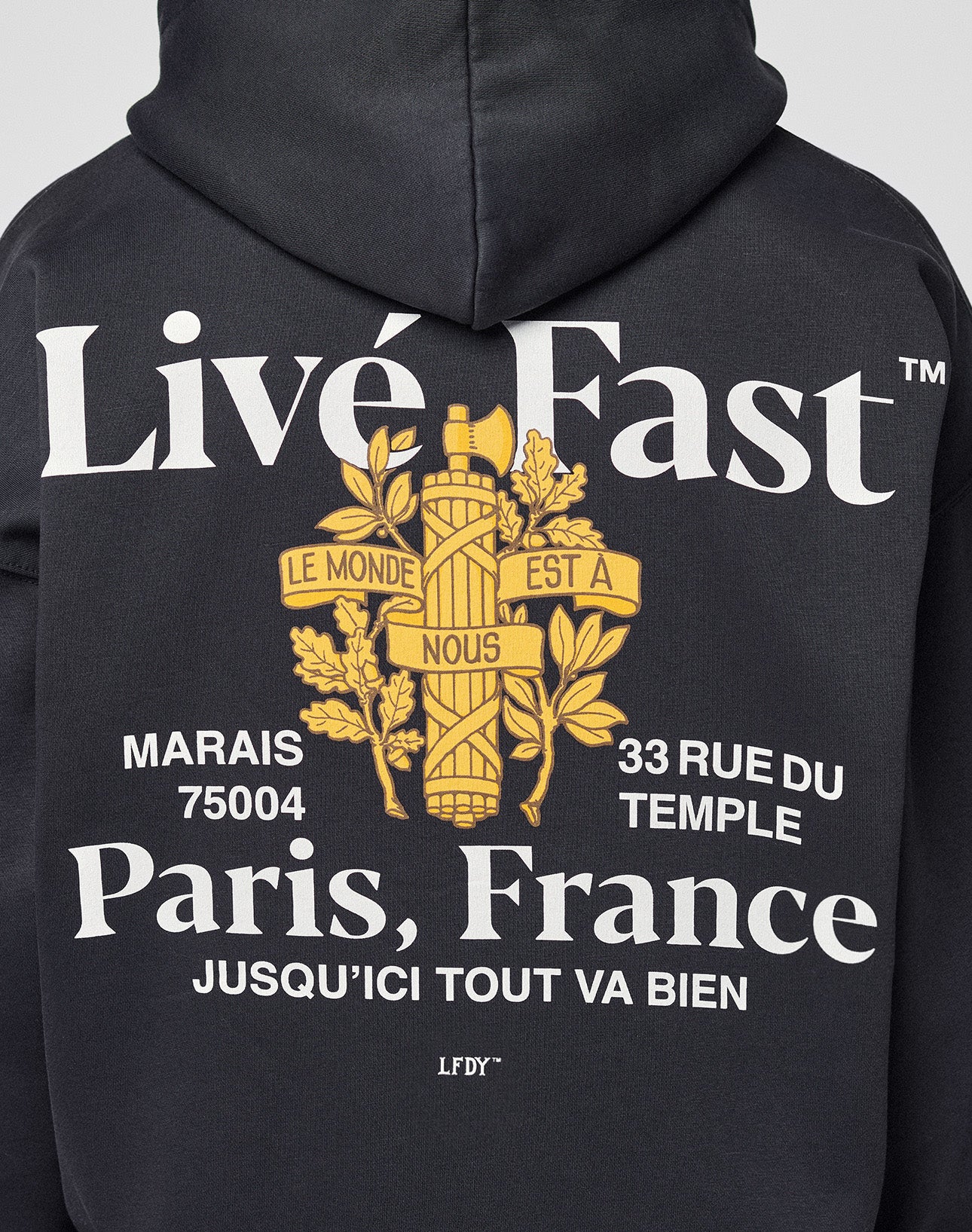 Back of the oversized LFDY Paris Hooded Zip by LIVE FAST DIE YOUNG in black cotton-poly features bold white “Live Fast, Paris, France” front and back prints with address details, a yellow fasces graphic, French phrases, and laurel leaves.