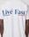 Back view of a person wearing the Live Fast Paris Tee by LIVE FAST DIE YOUNG, a white regular fit made from 100% Baumwolle, featuring bold Livé Fast™ blue text with red and blue underlines—a standout front and back design.