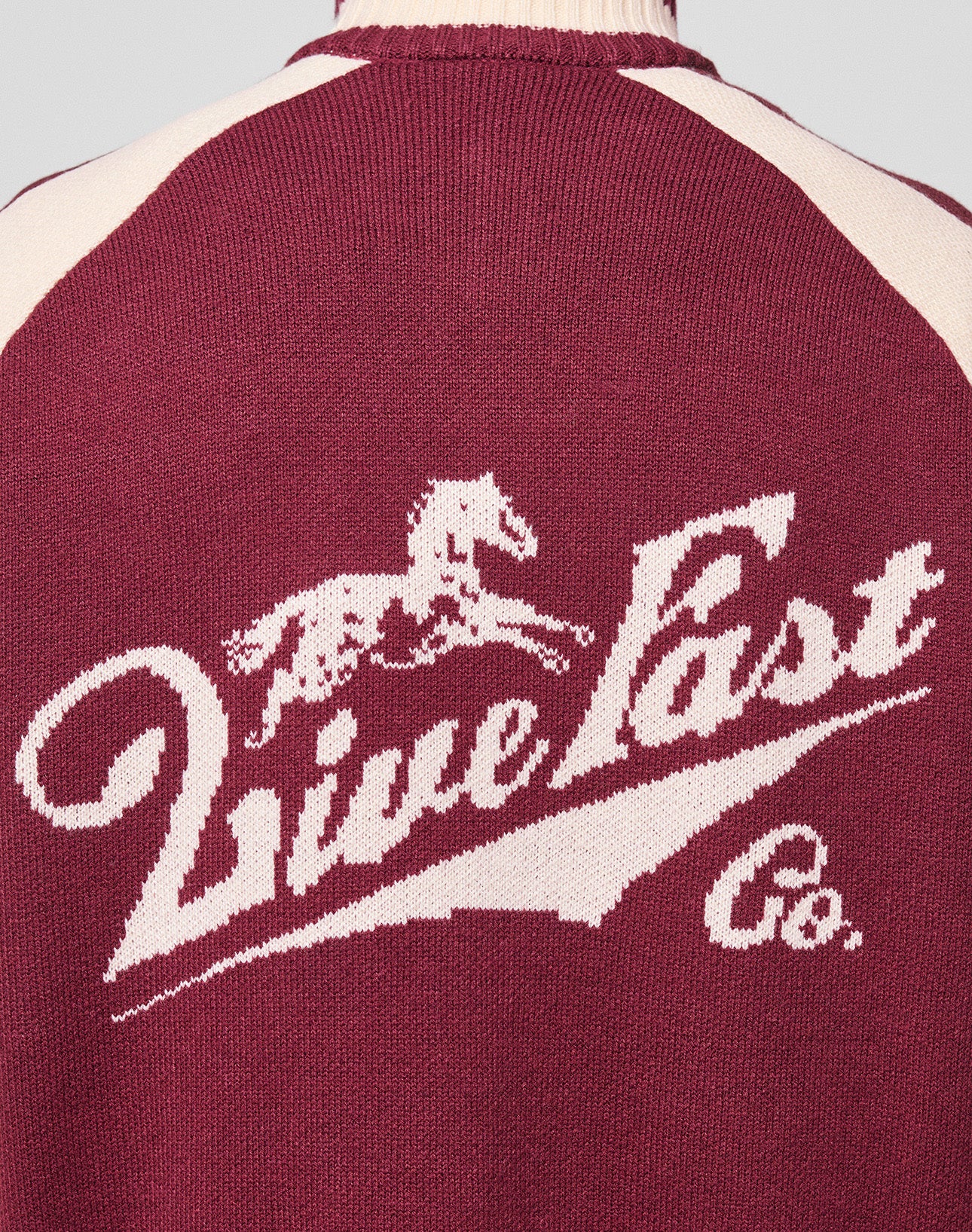 The back of the maroon and cream Boxy Knit Zip Jacket by LIVE FAST DIE YOUNG features intarsia-knit with a galloping horse graphic above bold, stylized “Live Fast Co.” text.