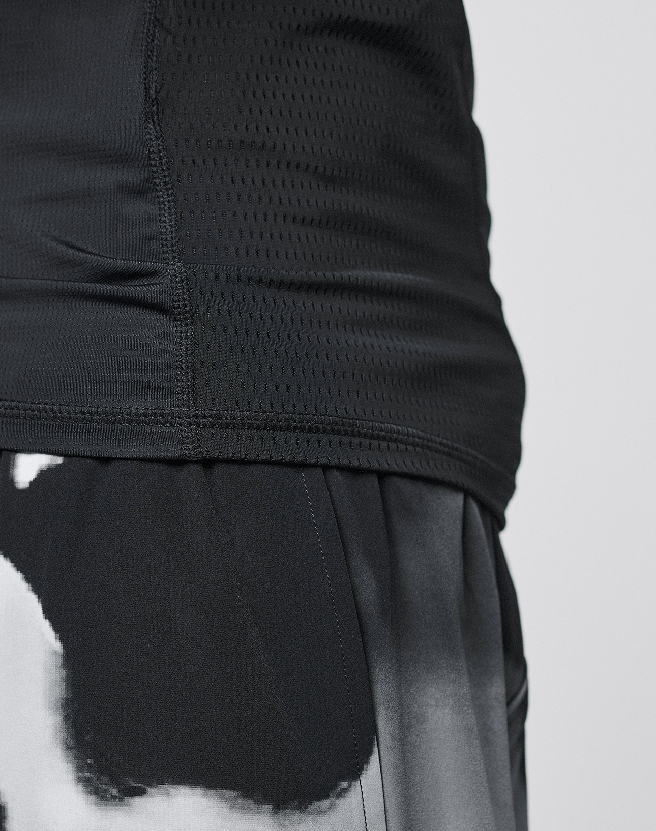 Close-up of a person's torso wearing the LFDY Performance Slim Tee by LIVE FAST DIE YOUNG, a black, perforated athletic top with a reflective logo print. Visible stitching and texture emphasize its slim fit and lightweight fabric.