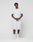 A man stands against a white background wearing the LIVE FAST DIE YOUNG Basic Chest Tee in light gray Baumwolle with matching Regular Fit shorts. He pairs the outfit with white socks and sneakers, hands clasped, gazing slightly to the side.