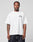 A man stands against a plain background, wearing the LIVE FAST DIE YOUNG Live Fast London Tee, an oversize fit 100% cotton white T-shirt with a front print, paired with dark baggy pants. He looks directly at the camera with a neutral expression.
