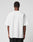 A person stands with their back to the camera, wearing the LIVE FAST DIE YOUNG Fuck Die Young Tee—a plain white 100% Baumwolle short-sleeve t-shirt—and black pants against a neutral light background.