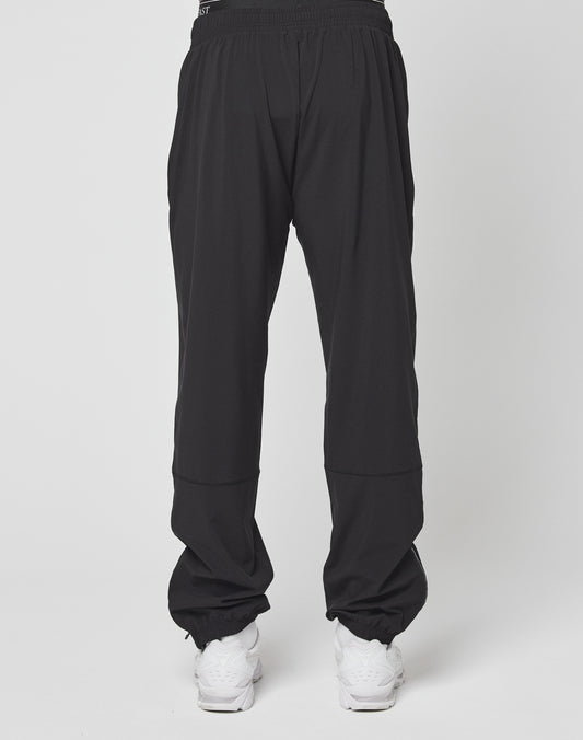 A person wearing LIVE FAST DIE YOUNG Live Fast Performance Running Pants in an oversize fit with an elastic waistband and white sneakers stands against a plain background, with the image focused on the back of the pants.