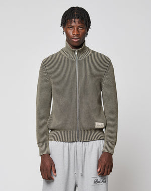 A man with short twisted hair wears the LFDY Knit Jacket from LIVE FAST DIE YOUNG in olive green and light gray sweatpants, standing against a plain white background.