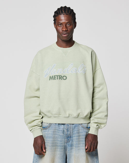 A man with braided hair wears a light green LFDY Vandals Sweater by LIVE FAST DIE YOUNG in Oversize Fit and light blue baggy jeans, standing against a plain white background.