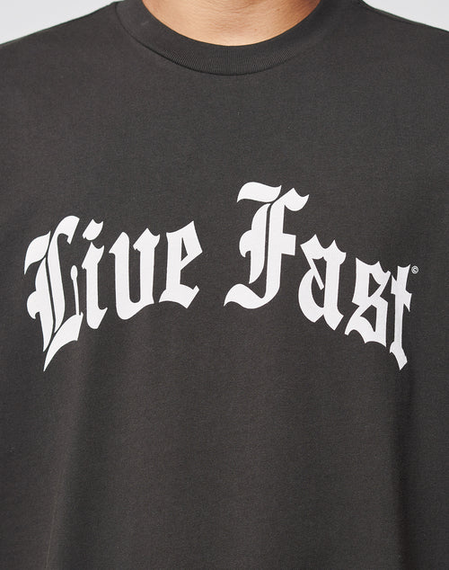 A person wears the Live Fast Fractured Tee by LIVE FAST DIE YOUNG—an oversize black t-shirt with a bold front print of Live Fast in large white Gothic-style letters.