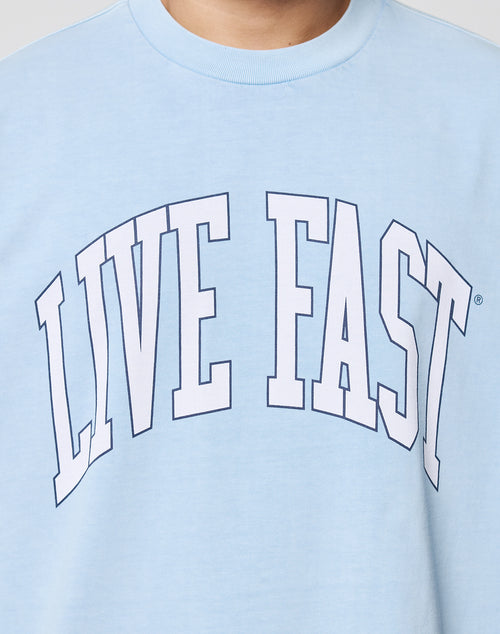 A person wears the Live Fast College Tee from LIVE FAST DIE YOUNG, featuring bold, white LIVE FAST letters across the chest. This oversize fit shirt is made from 100% Baumwolle and finished with a cool Vintagewaschung.
