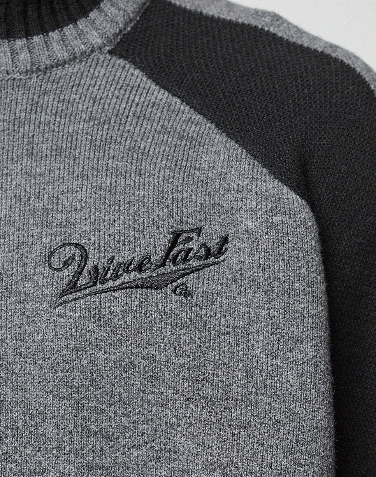 Close-up of the Boxy Knit Zip Jacket by LIVE FAST DIE YOUNG, in gray with black raglan sleeves and collar, featuring "Live Fast" embroidered in black cursive on the chest.