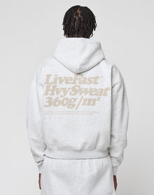A person with braided hair is seen from the back wearing an oversize fit light gray Basic 360 Hooded and sweatpants by LIVE FAST DIE YOUNG, featuring a bold beige “Live Fast Hyv Sweat 360g/m²” backprint. | model