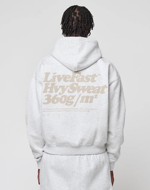 A person with braided hair is seen from the back wearing an oversize fit light gray Basic 360 Hooded and sweatpants by LIVE FAST DIE YOUNG, featuring a bold beige “Live Fast Hyv Sweat 360g/m²” backprint.