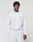 A man stands against a plain background, wearing the LIVE FAST DIE YOUNG Basic +49 Chest Sweater in an oversize fit, light gray cotton with a small left chest print, paired with matching sweatpants. He has short curly hair and a neutral expression.