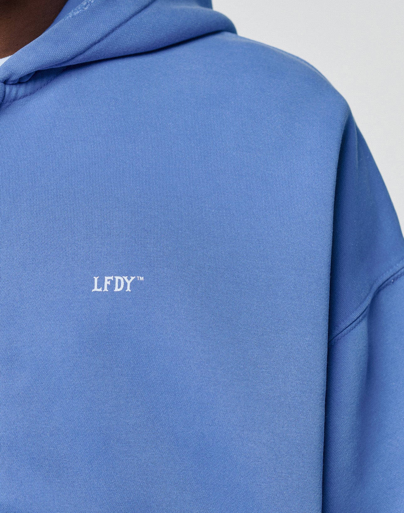 Close-up of the LIVE FAST DIE YOUNG Basic Hooded Zip in light blue with a faded look, bold white LFDY™ logo on the chest, and details highlighting its oversized fit across shoulders and hood.
