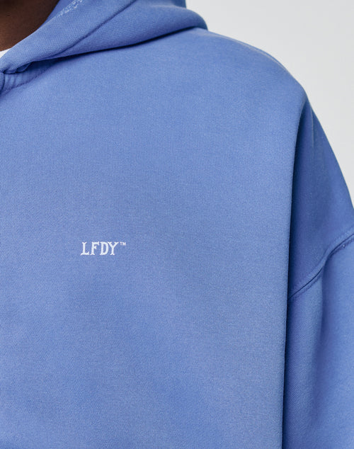 A close-up of a person wearing the LIVE FAST DIE YOUNG Basic Hooded Zip in light blue. The hoodie features soft fabric with a handgefertigter Fade-Effekt and subtle distressings on the hood for unique character.