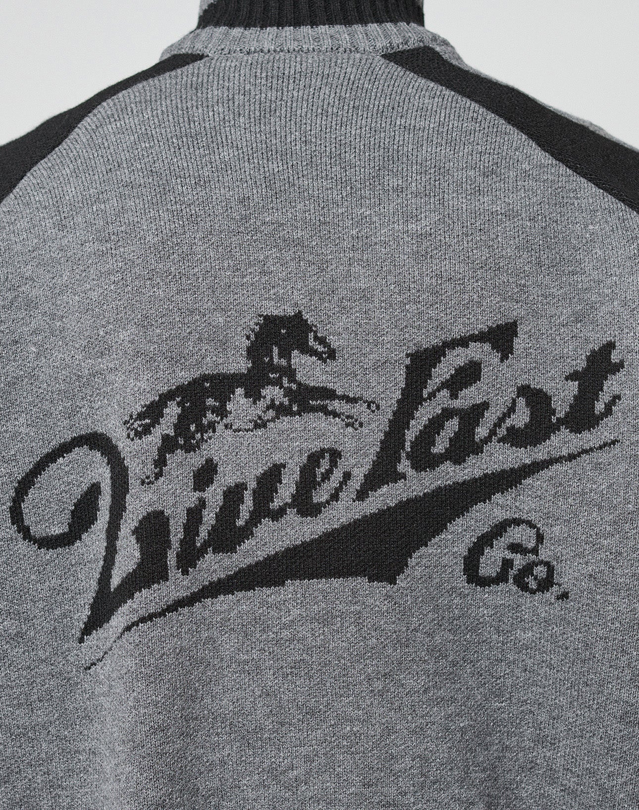 A close-up of the back of the Boxy Knit Zip Jacket by LIVE FAST DIE YOUNG, featuring an oversized gray fit with black "Live Fast Co." text and an intarsia-knit running horse above.
