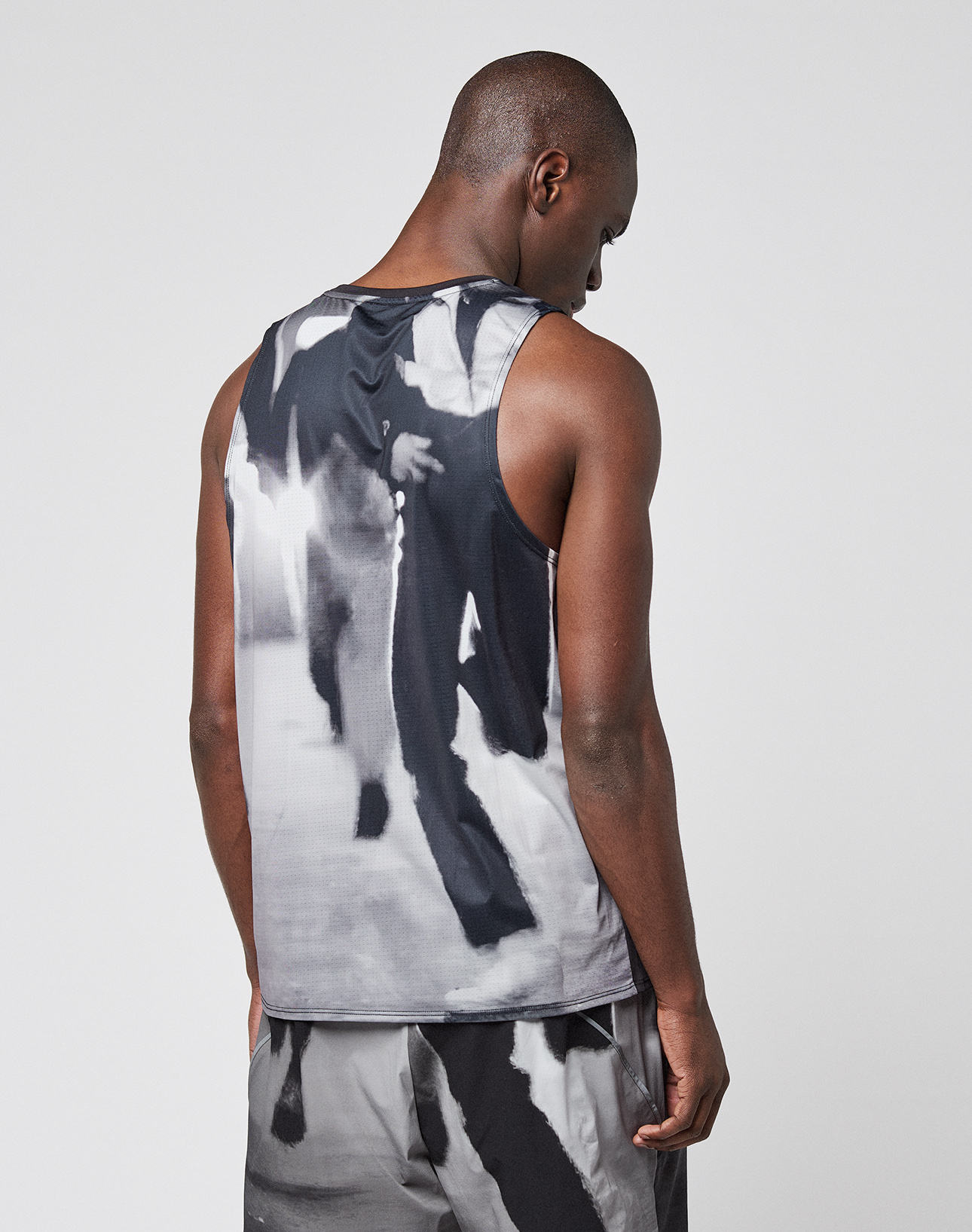 A person stands facing away from the camera, wearing a LIVE FAST DIE YOUNG LFDY Performance Tank and shorts with a black, white, and gray abstract pattern against a plain light background.