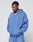 A man in an oversize fit blue LIVE FAST DIE YOUNG Basic Hooded Zip and matching sweatpants stands with his hands in his pockets, looking down against a plain light gray background.