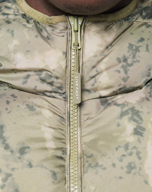 Close-up of the Live Fast Puffer Jacket by LIVE FAST DIE YOUNG, featuring a light camo pattern in green and beige, a zipper pull printed with LIVE FAST, and wasserabweisendes material for extra protection.