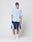 A person stands against a plain background wearing a blue headwrap, LIVE FAST DIE YOUNG’s Live Fast College Tee in light blue with LIVE FAST printed on it, dark blue athletic shorts with light blue accents, white socks, and white sneakers.