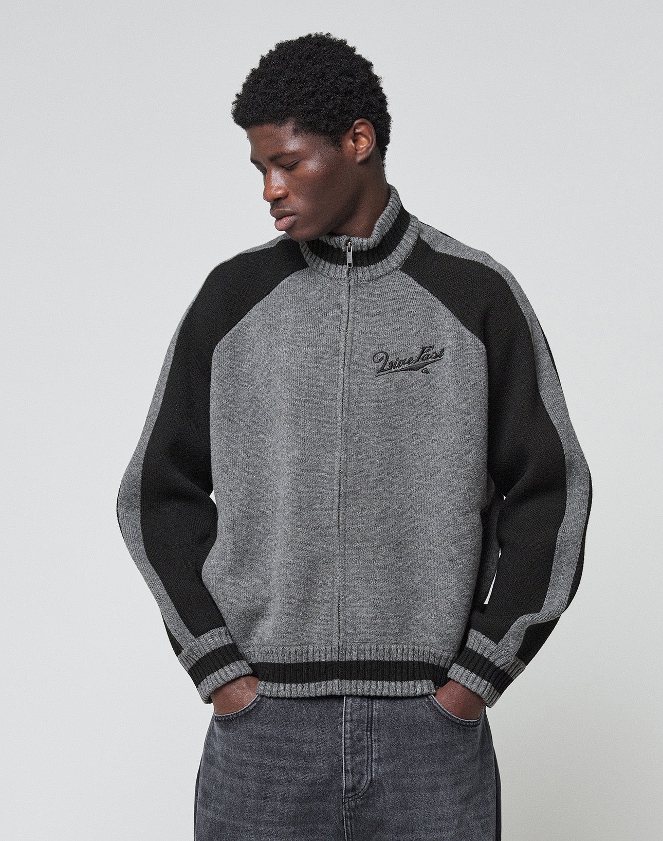 A person wears a gray and black Boxy Knit Zip Jacket by LIVE FAST DIE YOUNG, featuring Raglan sleeves and an oversize fit, with hands in pockets against a light gray background. "Diesel" is embroidered on the chest.
