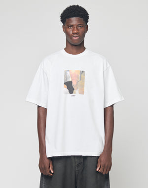 A man stands against a plain background wearing the LFDY Sharkhunter Tee by LIVE FAST DIE YOUNG, an oversize white 100% Baumwolle T-shirt featuring a blurry rectangle graphic and LFYT text on the front, paired with dark baggy jeans.