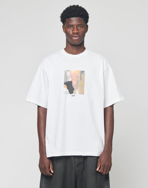 A man stands against a plain background wearing the LFDY Sharkhunter Tee by LIVE FAST DIE YOUNG, an oversize white 100% Baumwolle T-shirt featuring a blurry rectangle graphic and LFYT text on the front, paired with dark baggy jeans.