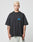 A person with short bleached blond hair wears the LFDY 4 Ever Tee from LIVE FAST DIE YOUNG—an oversized black cotton t-shirt with LIVE FAST in blue on the chest, standing against a plain light background with tattoos visible on both arms.