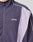 A close-up of a person wearing the LIVE FAST DIE YOUNG Basic Nylon Trackjacket in purple with light lavender and white accents. The regular fit has side entry pockets and Live Fast embroidered in white script on the left chest.