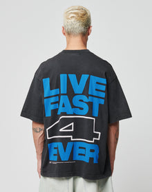 A person with short, bleached hair wears the LIVE FAST DIE YOUNG LFDY 4 Ever Tee, an oversize black Baumwolle T-shirt with a bold blue and white LIVE FAST 4 EVER backprint, as they face away from the camera. | model