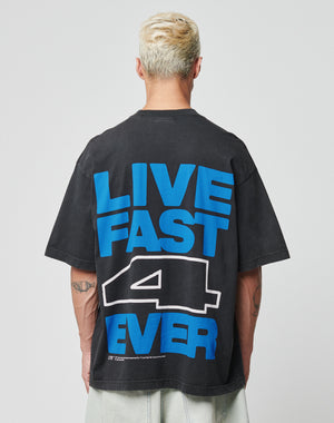 A person with short, bleached hair wears the LIVE FAST DIE YOUNG LFDY 4 Ever Tee, an oversize black Baumwolle T-shirt with a bold blue and white LIVE FAST 4 EVER backprint, as they face away from the camera.