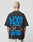 A person with short, bleached hair wears the LIVE FAST DIE YOUNG LFDY 4 Ever Tee, an oversize black Baumwolle T-shirt with a bold blue and white LIVE FAST 4 EVER backprint, as they face away from the camera.