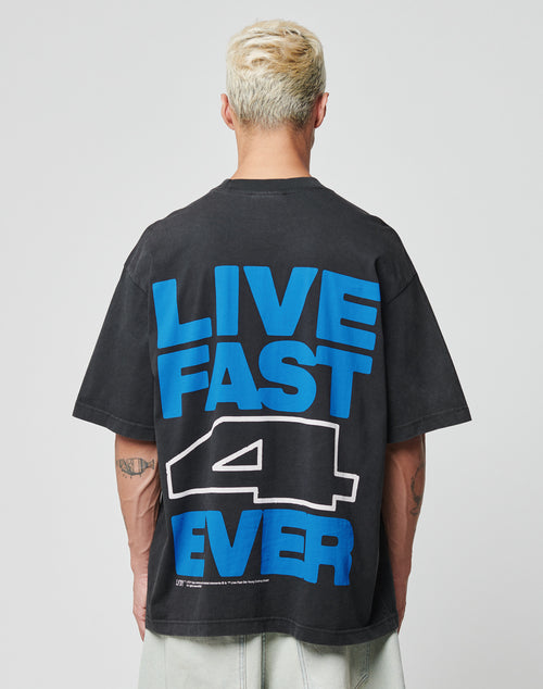 A person with short, bleached hair wears the LIVE FAST DIE YOUNG LFDY 4 Ever Tee, an oversize black Baumwolle T-shirt with a bold blue and white LIVE FAST 4 EVER backprint, as they face away from the camera.