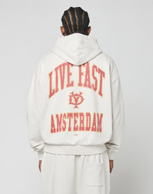 A person with braided hair is seen from behind wearing the LIVE FAST DIE YOUNG Live Fast Amsterdam Hooded in light gray, featuring an oversize fit and bold red and yellow LIVE FAST AMSTERDAM text with a small central logo front and back. | model