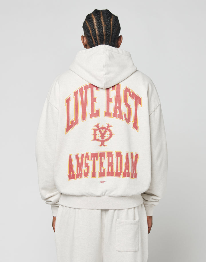 A person with braided hair is seen from behind wearing the LIVE FAST DIE YOUNG Live Fast Amsterdam Hooded in light gray, featuring an oversize fit and bold red and yellow LIVE FAST AMSTERDAM text with a small central logo front and back. | model
